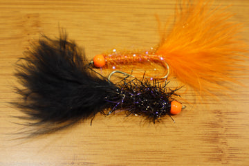 Fly fishing lure with black and orange feathers on a wooden surface
