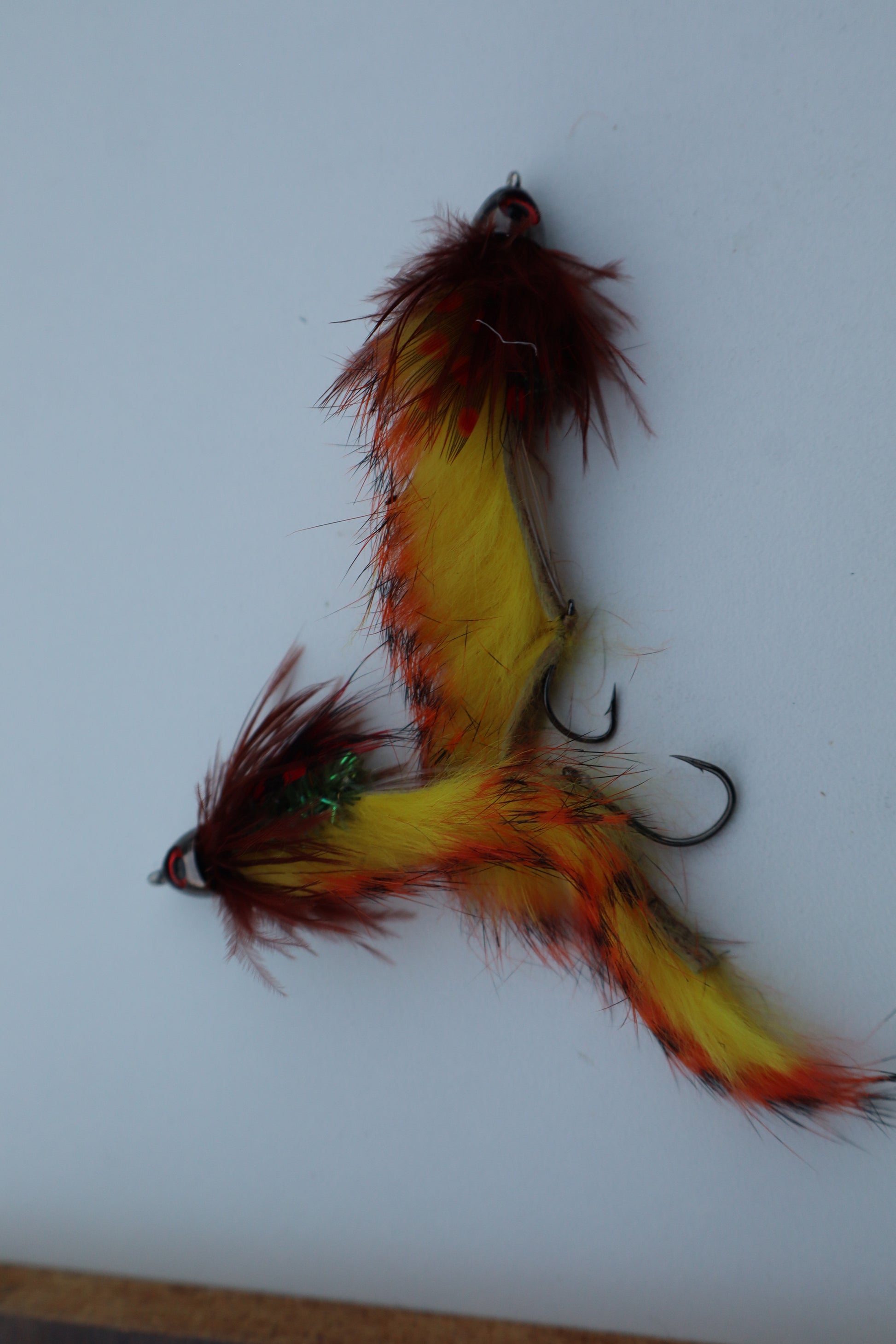 Fishing fly with red, yellow, and black feathers on a white background