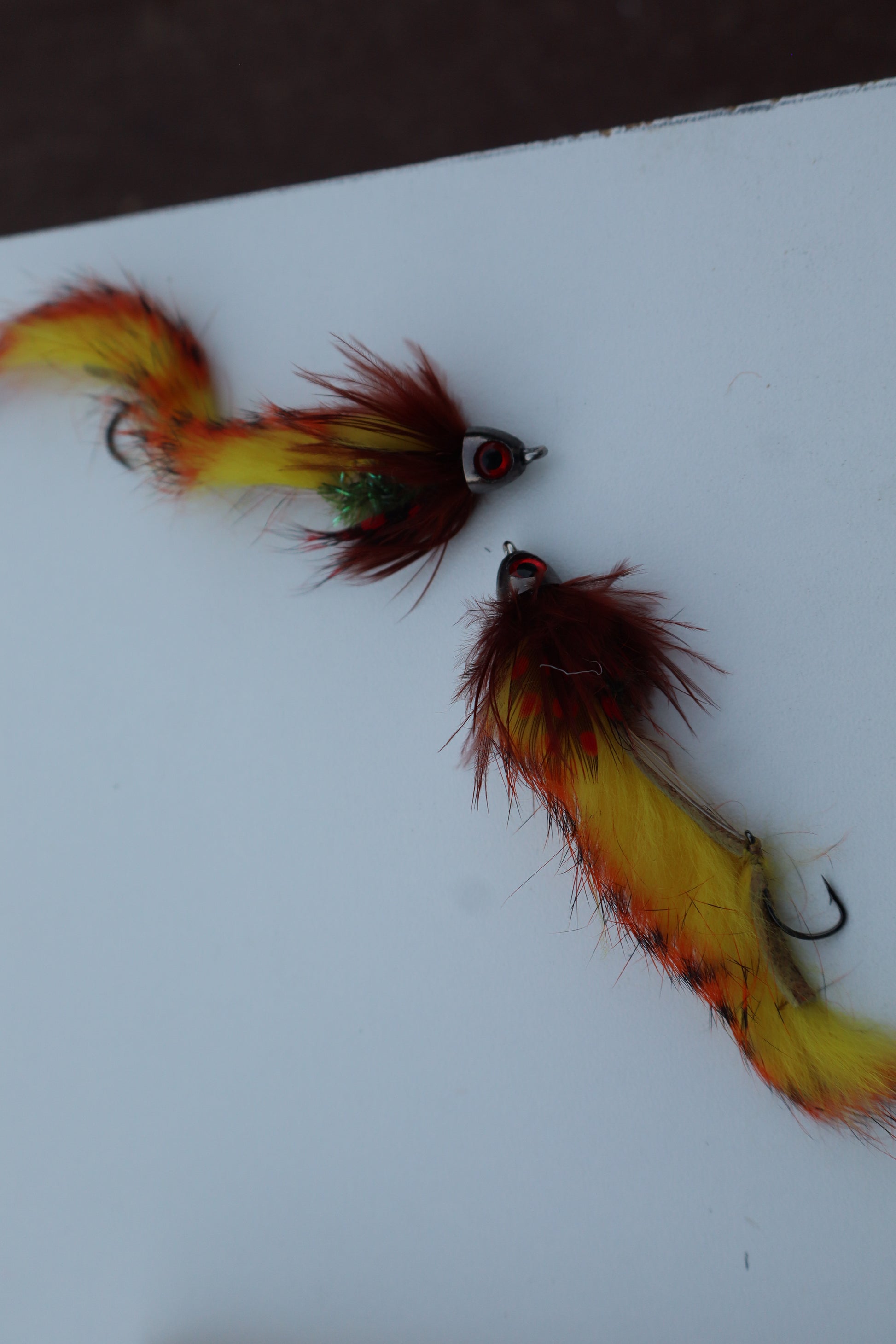 Two red and yellow fly fishing lures on a white background